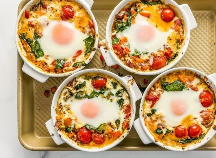 Baked feta eggs with fresh tomatoes and spinach in a ceramic dish