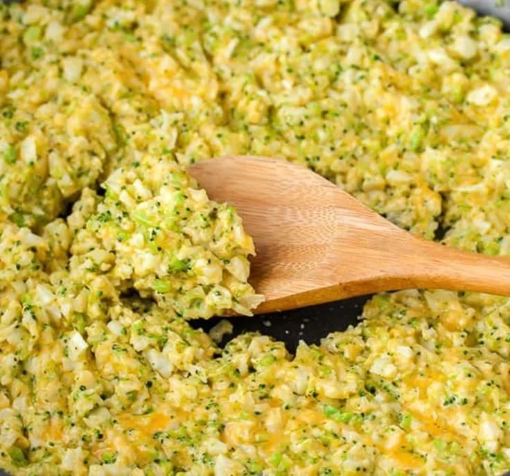 Cheesy broccoli cauliflower rice in a bowl, topped with melted cheese and herbs.