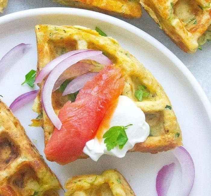 Cheddar zucchini waffles fresh from the waffle maker, topped with herbs.