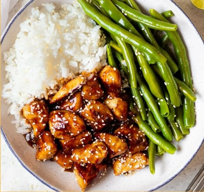 Healthy homemade sesame chicken garnished with sesame seeds and vegetables.