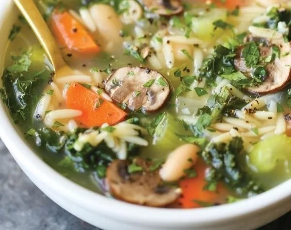 A healthy bowl of chicken soup with fresh vegetables and herbs.