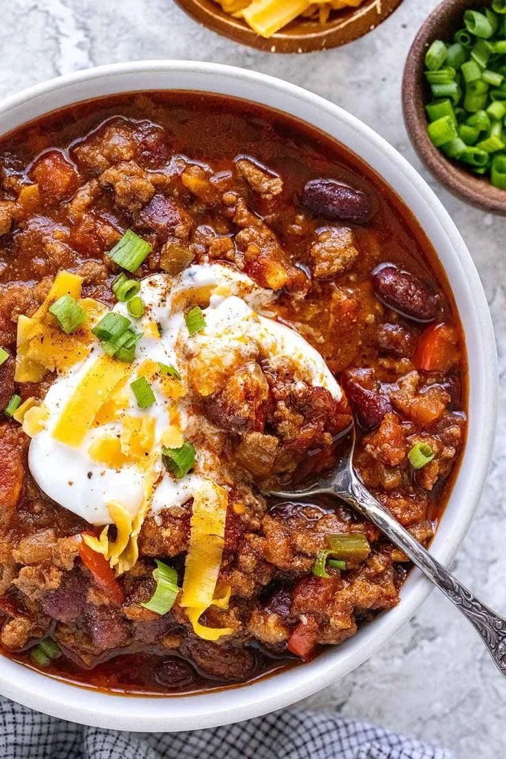 Bowl of homemade chili topped with cheese and herbs, perfect for sharing.